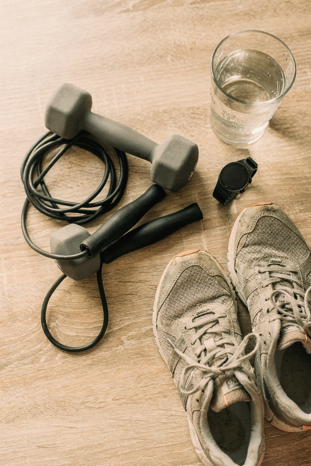 A jump rope coiled loosely, a pair of dumbbells, running shoes, a heart rate monitor watch, and a glass of water. , no faces, no hands