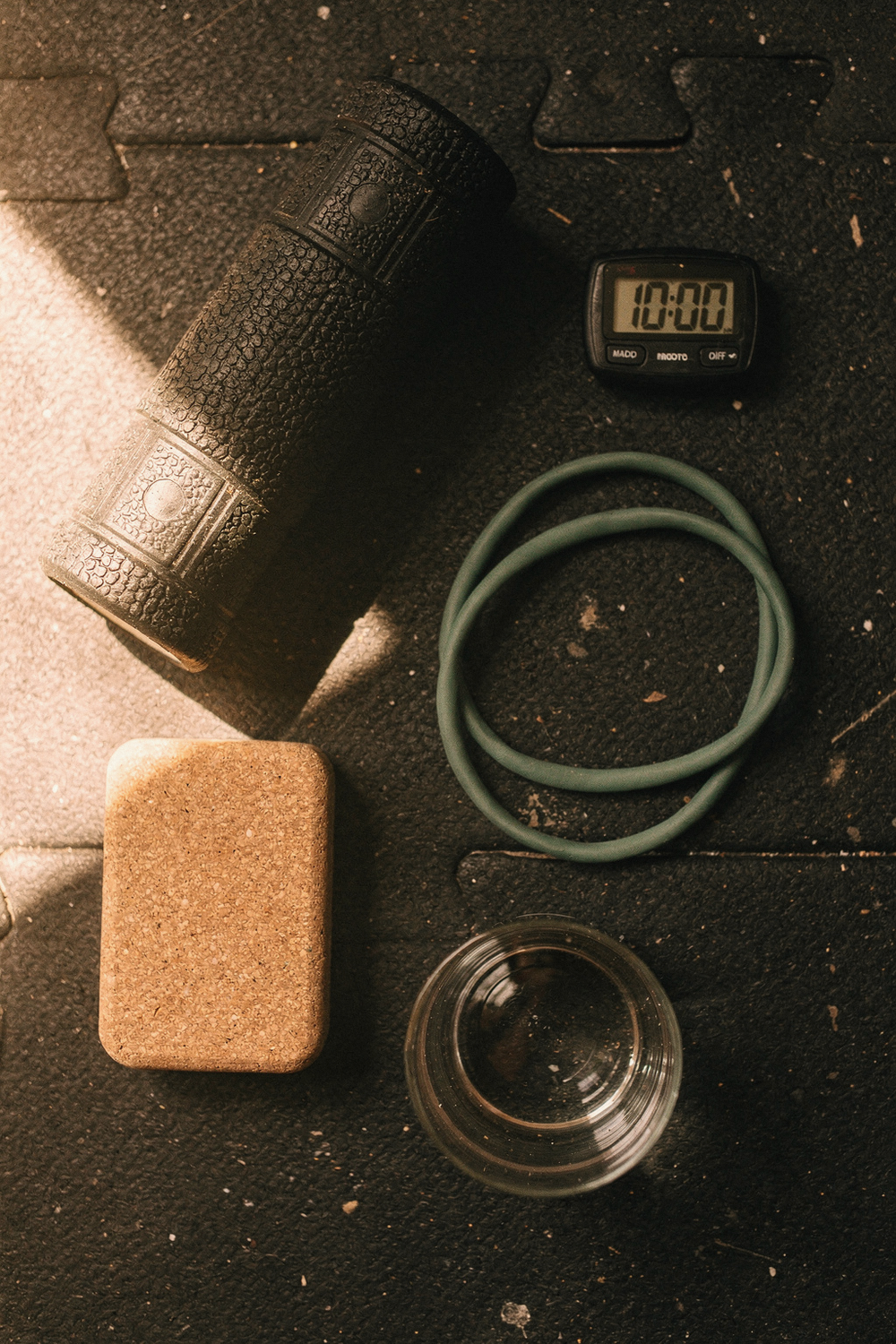 A foam roller, a resistance band, a yoga block, a timer showing 10 minutes, a glass of water. Grounded, accessible, no-excuses. , no faces, no hands