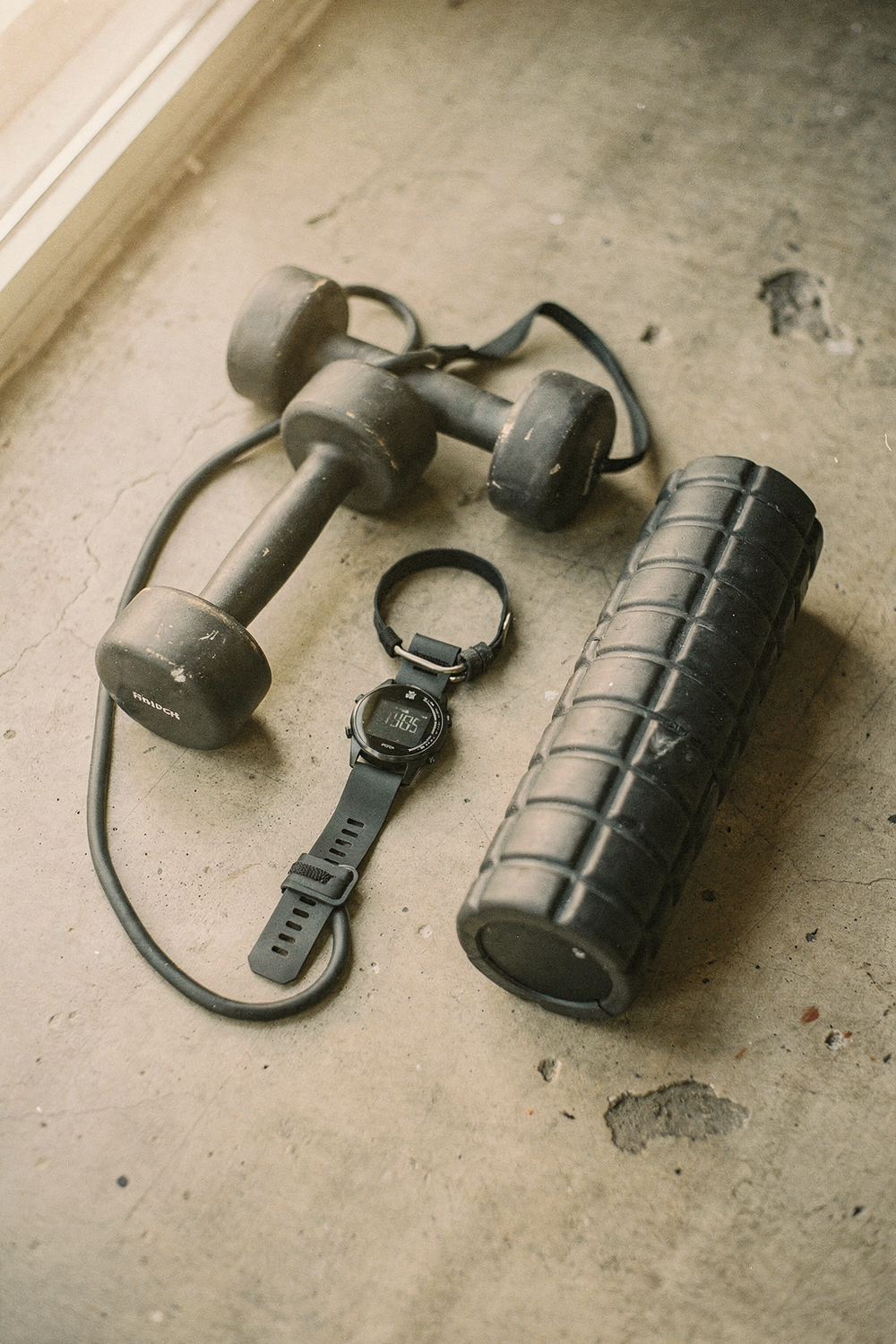 A heart rate monitor watch, a pair of dumbbells, a resistance band, and a foam roller arranged casually