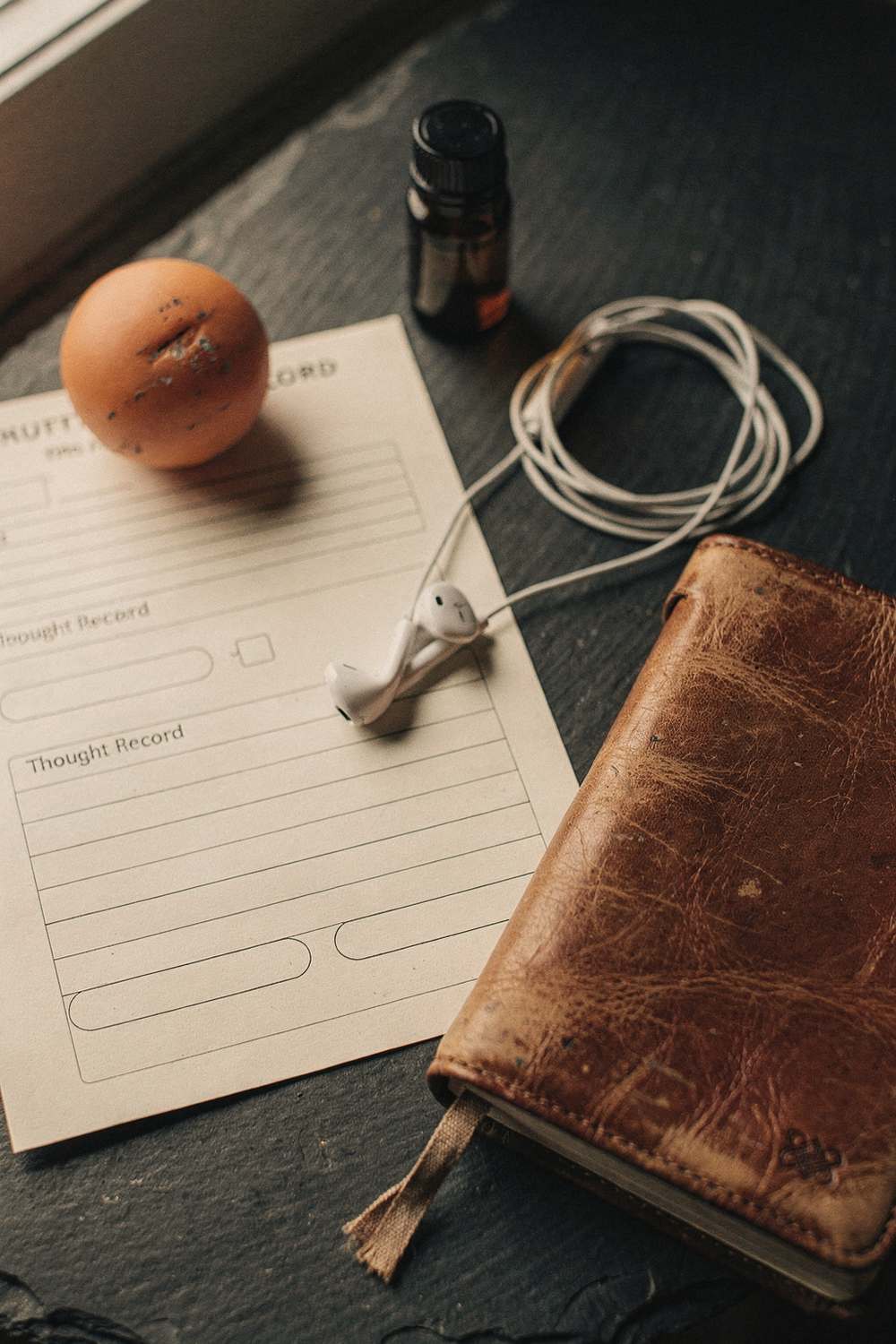 A thought record worksheet, a stress ball, a small essential oil bottle, a pair of earbuds, and a worn journal with a bookmark