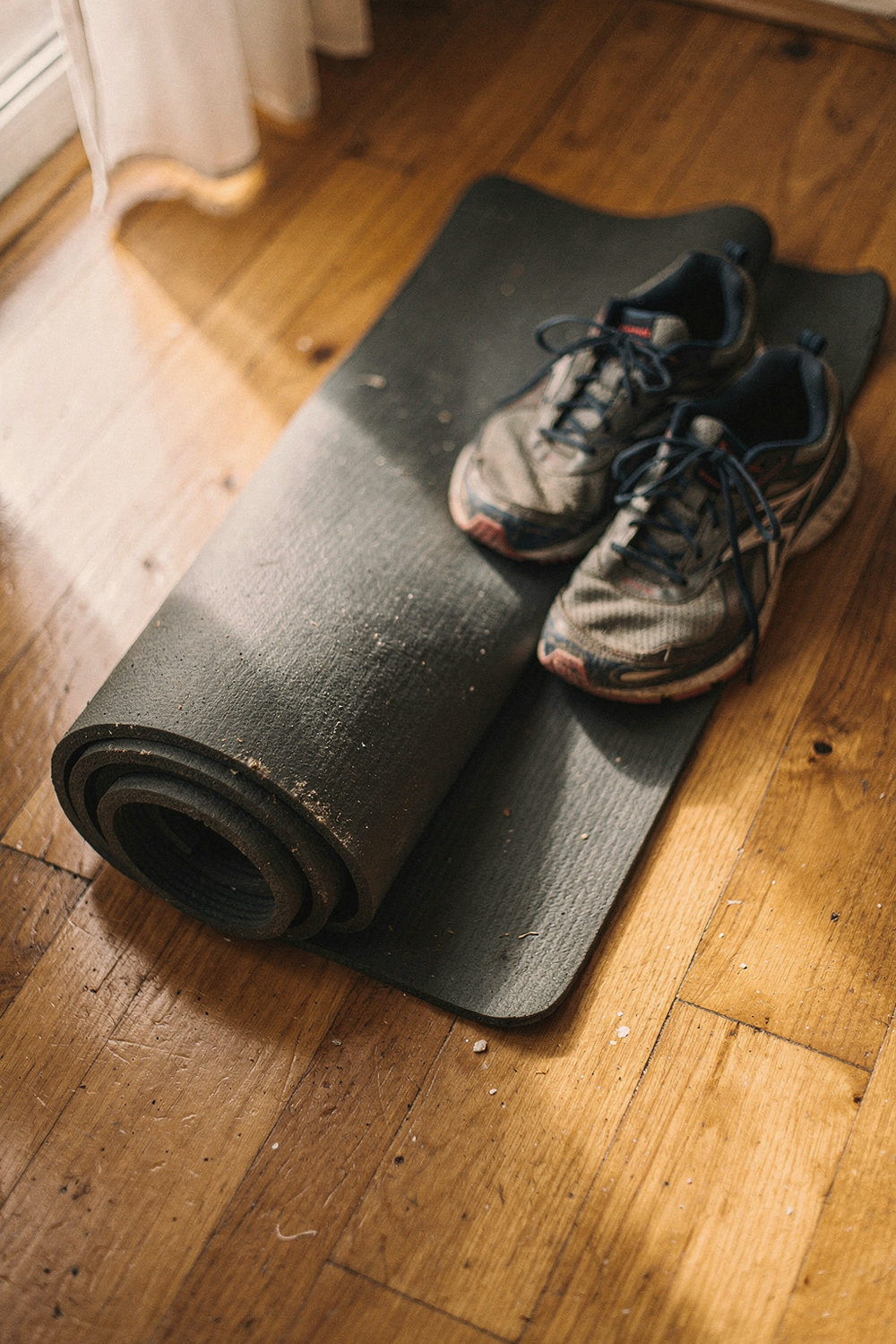 Yoga mat partially rolled up next to running shoes on a hardwood floor
