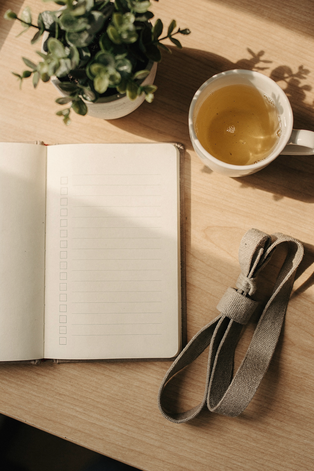 Notebook with a checklist, herbal tea, stretching strap, and a small plant on a wooden desk