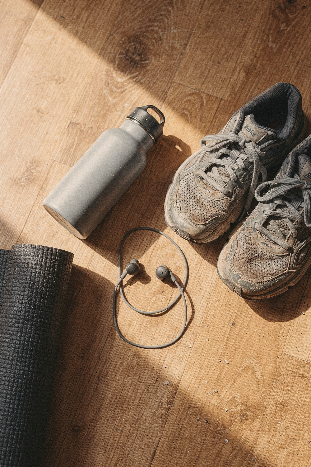 Running shoes, yoga mat corner, water bottle, and a pair of earbuds loosely placed