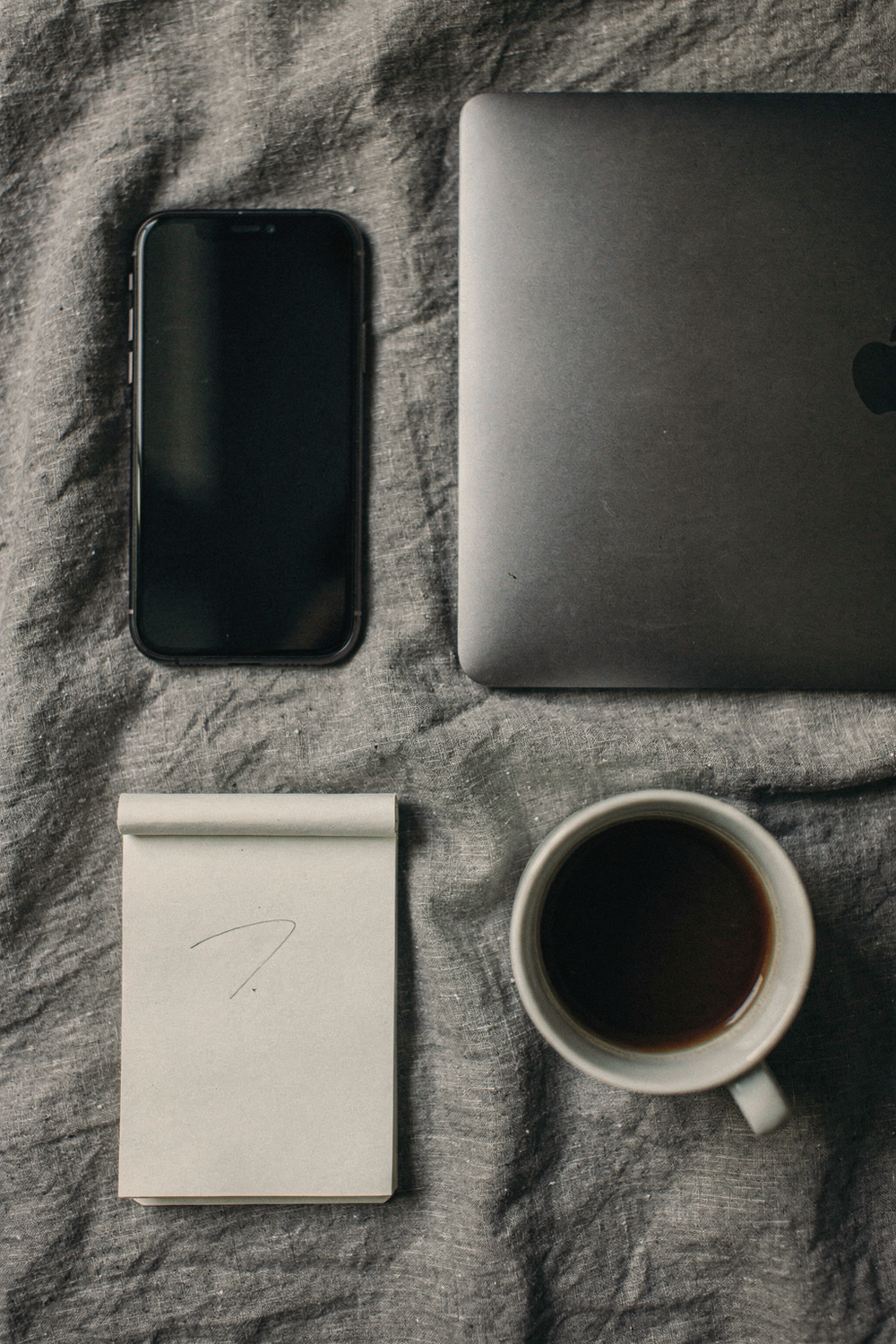 Smartphone face-down, closed laptop, untouched coffee cup, small notepad with one word written