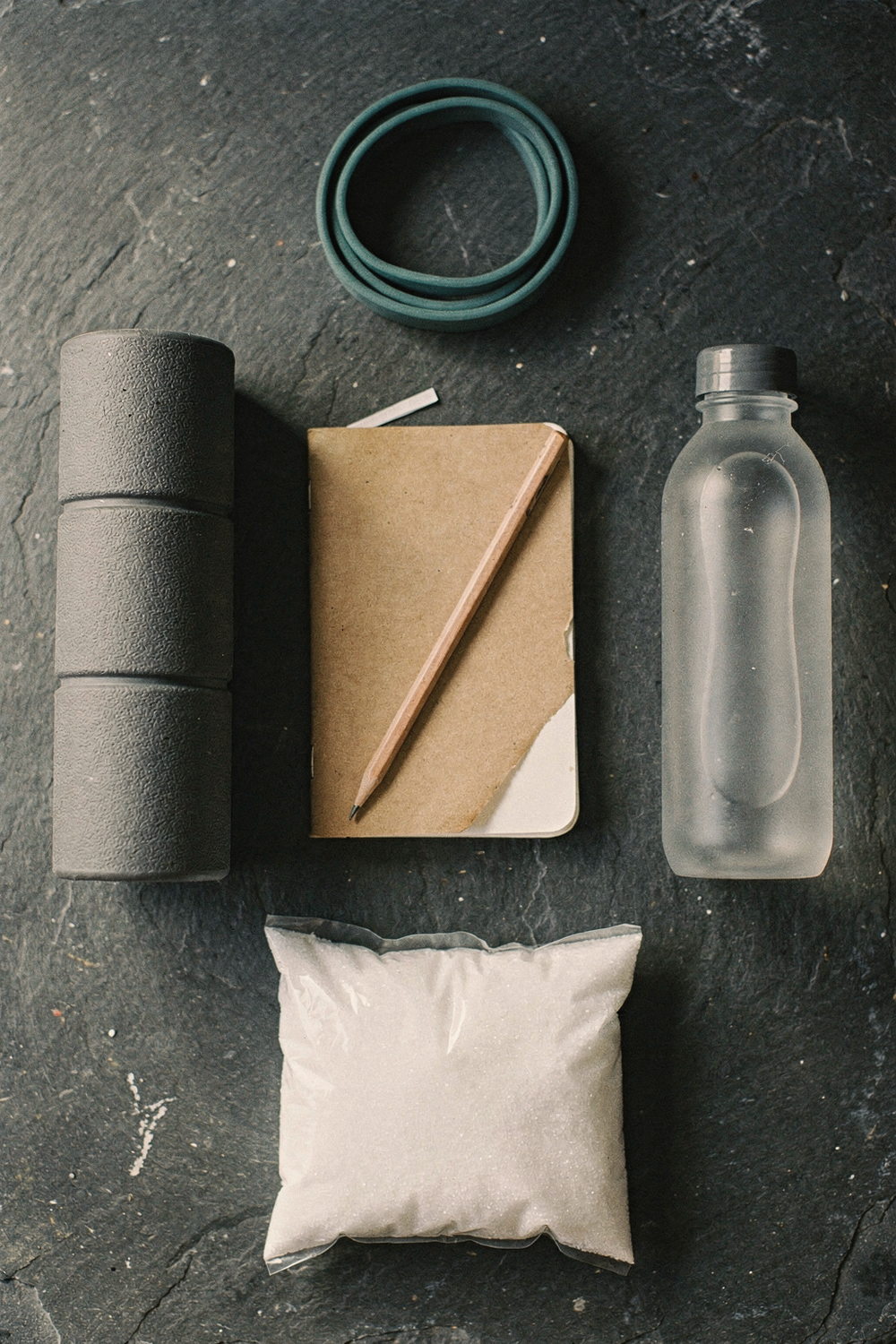 A foam roller, a small notebook with a pencil, a water bottle, a resistance band, and a bag of epsom salts. , no faces, no hands