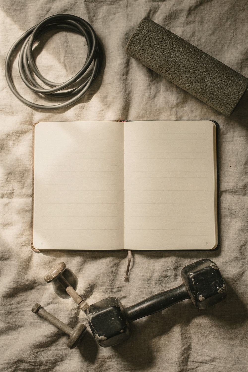 A movement journal open to a page with simple handwritten notes, a foam roller, a resistance band, and a small dumbbell set to one side. , no text, no logos
