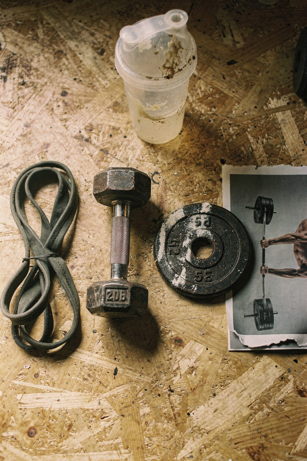 Resistance band, dumbbell, weight plate with chalk, and a fitness magazine page arranged on plywood