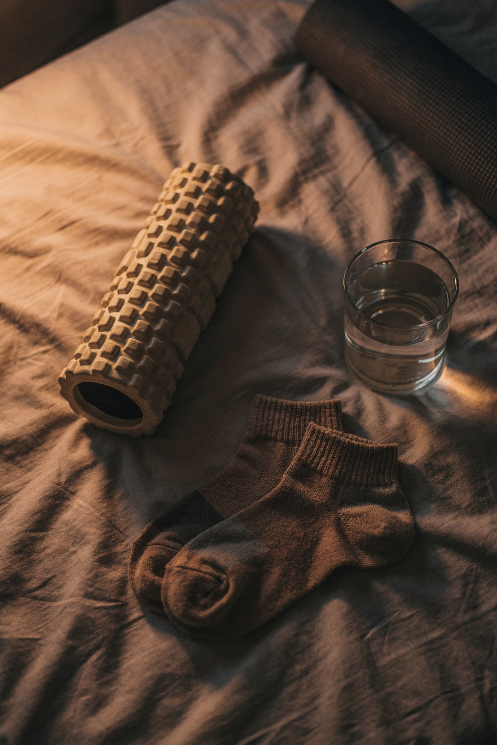 A foam roller, a rolled yoga mat corner, a pair of cozy socks, and a glass of water. , no text, no logos