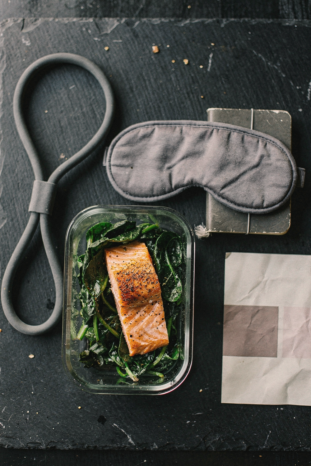 A resistance band, a container of salmon and leafy greens, a sleep mask, a small journal, and a community event flyer