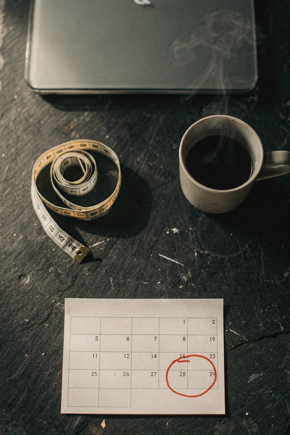 Bathroom scale, measuring tape, a calendar with the third month circled in red, and a cup of black coffee