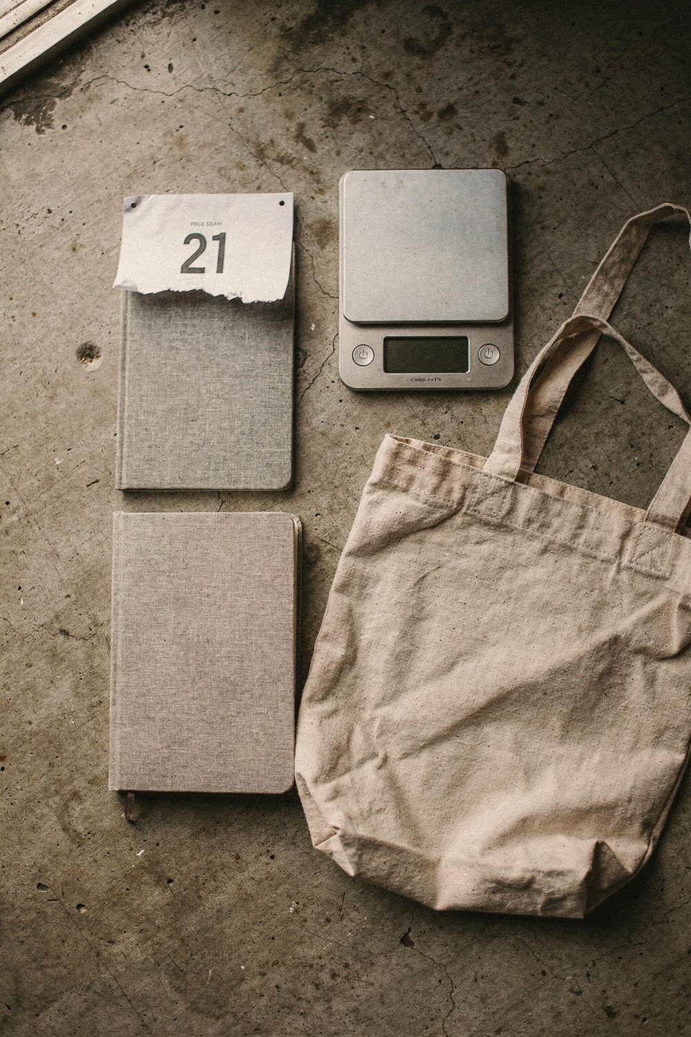 A torn-off calendar page showing day 21, a full yearly planner, a kitchen scale, a journal, and a reusable grocery bag