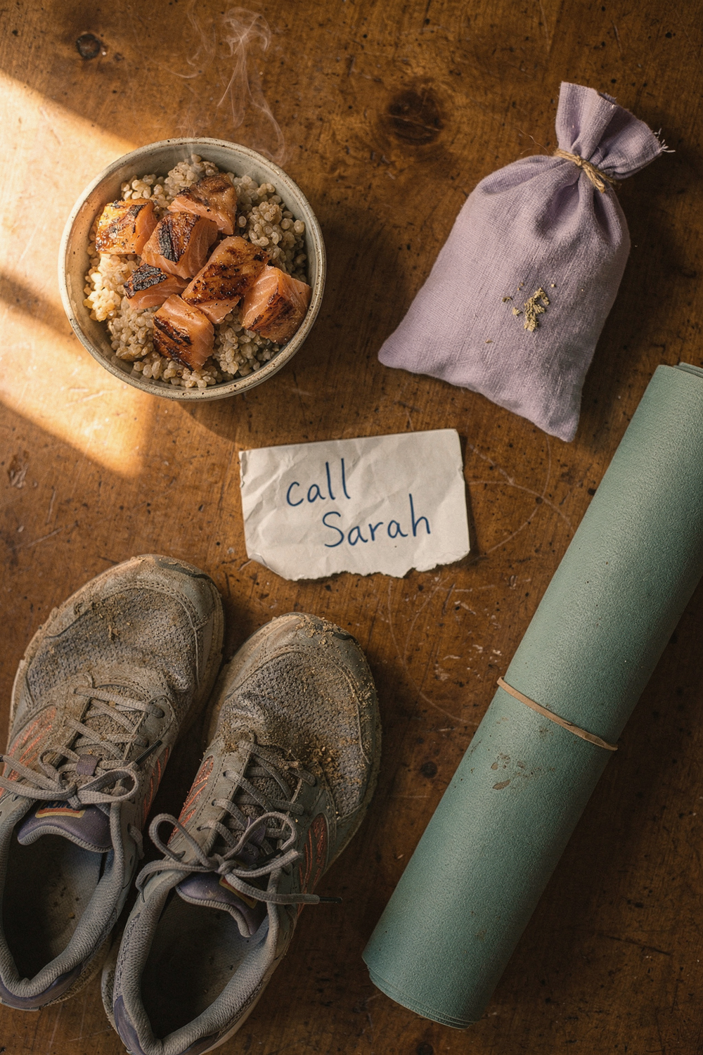 Five objects in a circle: salmon bowl, lavender sachet, running shoes, yoga mat, and a handwritten note on a wood table
