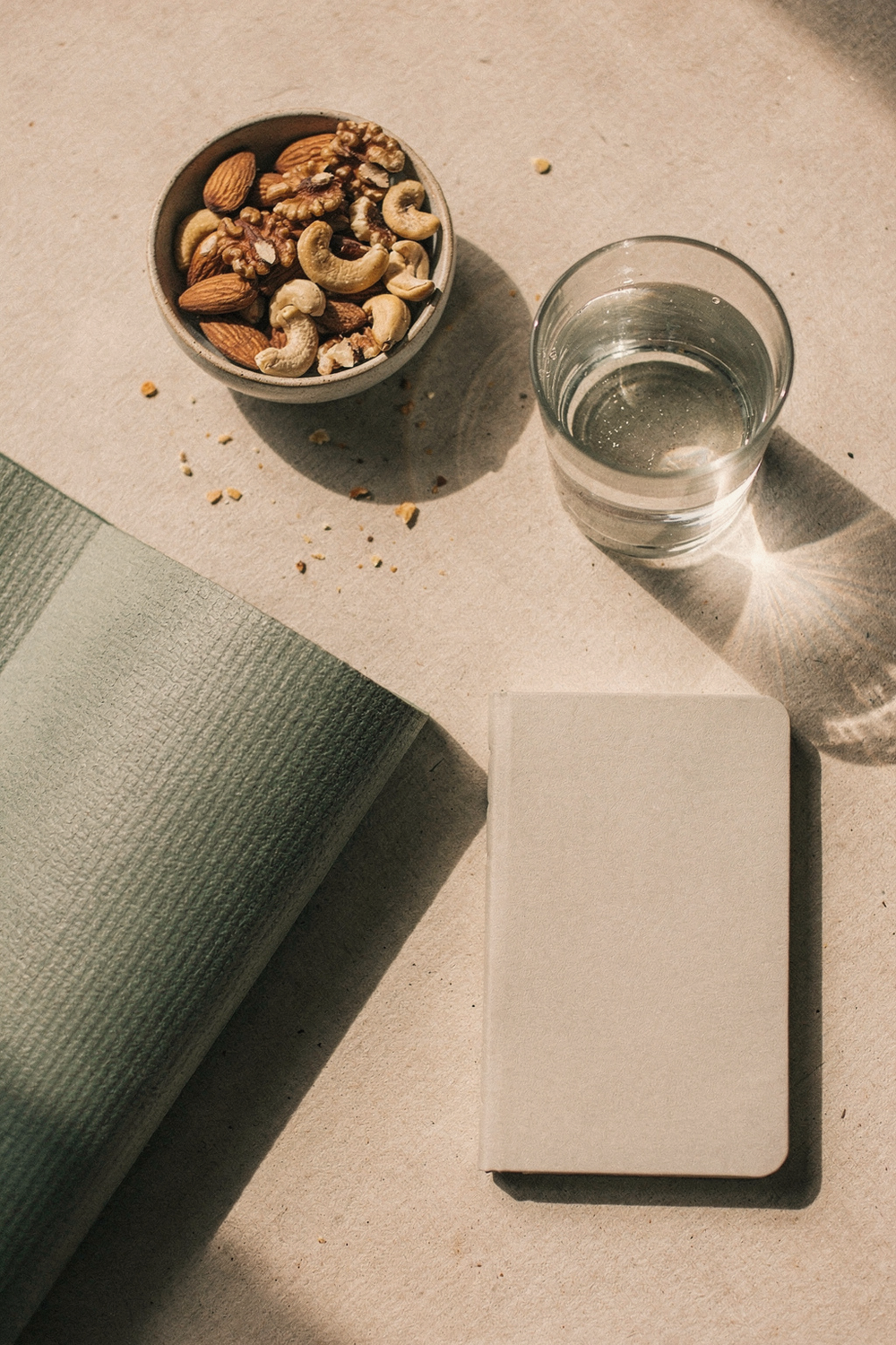 Yoga mat corner, a bowl of nuts, a water glass, and a small journal on a light surface